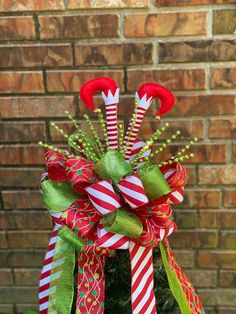 a red and green christmas bow with candy canes on it's top, sitting in front of a brick wall