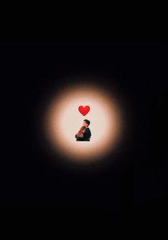 a person sitting in the dark with a red heart above their head