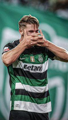 a soccer player holding his hands to his face while standing in front of a green and white background