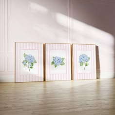 three framed pictures with blue flowers in them on a wooden floor next to a pink wall