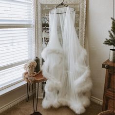 a room with a bed, window and white curtain in the corner next to a small table