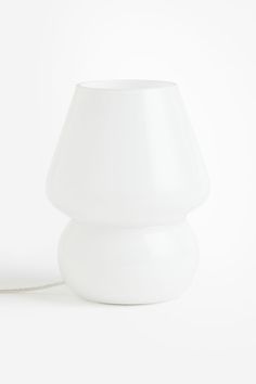 a white table lamp sitting on top of a white floor next to a light bulb