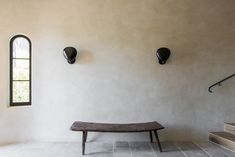 a bench sitting in the middle of a room next to a window and stairs with two black vases on each side