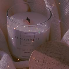 a white candle sitting on top of a pink blanket next to a wooden plaque that reads i candies the scent