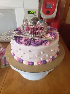 there is a pink cake with purple flowers and a crown on top