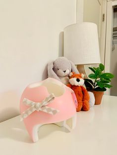 two stuffed animals sitting next to each other on a white table with a lamp and potted plant