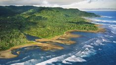 an aerial view of the ocean and land with waves crashing on the shore, surrounded by trees