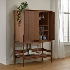 a wooden cabinet with wine glasses and bottles on it in front of a large window