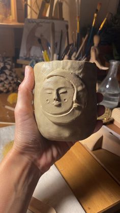 a person holding up a clay cup with a face on it