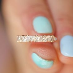 a woman's hand holding a gold ring with three diamonds on it and a blue manicure