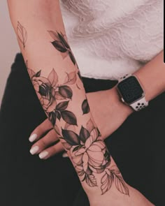 a woman's arm with flowers and leaves tattooed on the wrist, holding an apple watch