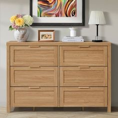 a wooden dresser with two vases on top of it next to a framed painting