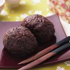 two chocolate donuts on a plate with chopsticks