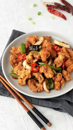 a white plate topped with fried vegetables and chopsticks next to some red peppers