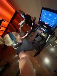 a woman on a stationary exercise bike with headphones in her ears looking at the screen