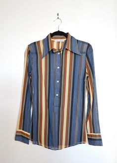 Make a bold statement with this striped button-up shirt from Dolce & Gabbana. This long-sleeve shirt is a perfect mix of retro charm and modern sophistication, featuring a striking blend of blue, brown, and beige tones. Half-placket front closure and zipper at side. Semi-sheer. Brand: Dolce & Gabbana Composition: 100% Cotton Size: IT 42 Summer Long Sleeve Blouse With Vertical Stripes, Long Sleeve Blouse With Vertical Stripes For Summer, Spring Long Sleeve Tops With Vertical Stripes, Spring Long Sleeve Blouse With Vertical Stripes, Fall Button-up Shirt With Striped Collar, Fall Long Sleeve Shirt With Striped Collar, Fall Long Sleeve Blouse With Striped Collar, Spring Striped Long Sleeve Blouse, Spring Blouse With Striped Long Sleeves