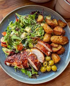 a blue plate topped with meat, salad and potatoes