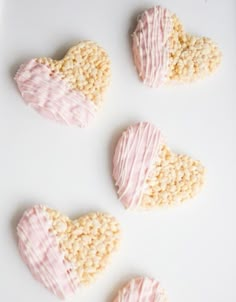 four heart shaped cookies are on a white plate with pink icing and sprinkles