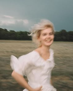 a woman running through a field with trees in the background