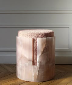 a marble stool sitting on top of a hard wood floor next to a white wall