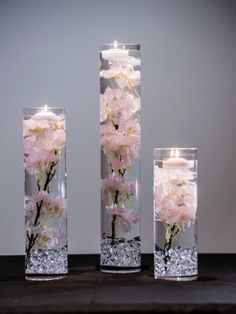 three tall vases with flowers in them on a table