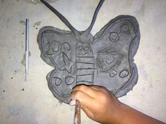 a child's hand is holding a pencil and drawing a butterfly shaped object on the ground