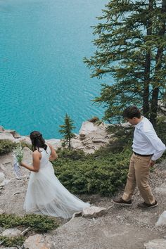 a man and woman standing on top of a mountain next to a body of water