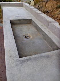 a concrete sink sitting on top of a brick walkway next to a hillside with trees