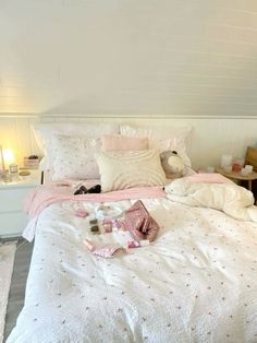 a white bed with pink and white comforter next to a night stand on the floor