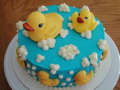 a blue cake with yellow rubber ducks on top and white clouds around the edges, sitting on a wooden table