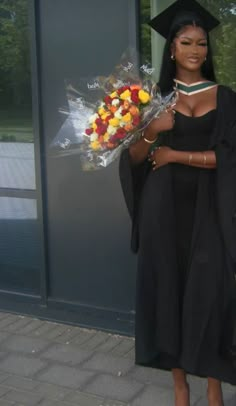 a woman wearing a graduation gown holding flowers and a bouquet in front of a building