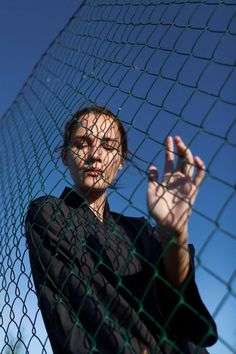 a woman standing behind a fence holding her hand up