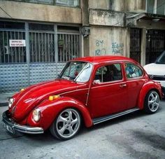 an old red car parked on the side of the road in front of a building