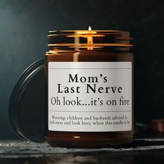 a candle that is sitting on top of a table next to a cup with the words, mom's last nerve oh look it's on fire