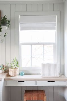 a white desk sitting under a window next to a potted plant on top of a wooden bench