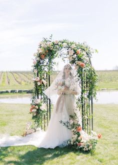 a woman in a wedding dress standing under an arch with flowers and greenery on it