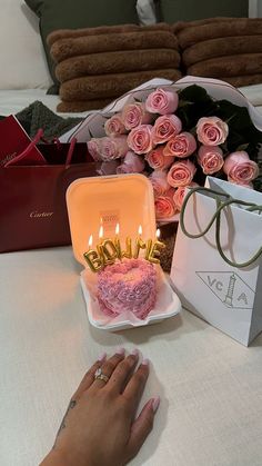 a woman's hand next to a birthday cake with candles on it and pink roses in the background