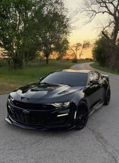 a black chevrolet camaro is parked on the road in front of some trees and grass