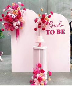 there is a wedding cake on top of a pedestal with flowers in the middle and bride to be sign behind it