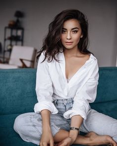 a woman in white shirt and jeans sitting on a blue couch with her legs crossed