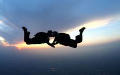 two people jumping into the air with their hands in each other's pockets as the sun sets behind them