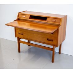 a wooden desk with two drawers and a drawer on the top, in front of a white wall