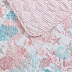 a pink and blue quilted bed with coral reef print on the bottom, along with white stripes