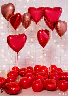 a bunch of red heart shaped balloons in front of a white brick wall with lights