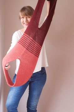 a woman holding a large knitted object in the air with one leg and two hands