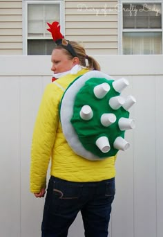 a woman in a yellow jacket with a green and white backpack on her back, standing next to a house