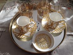 two cups and saucers are sitting on a tray with gold trimmings around them