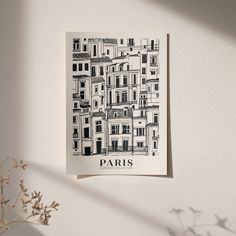 a black and white drawing of paris hangs on the wall next to a vase with flowers