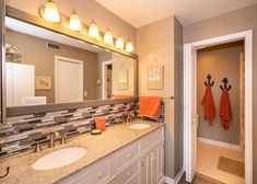 a bathroom with two sinks and orange towels on the rack above it's mirror