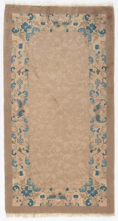 a beige rug with blue flowers on the bottom and brown border, in front of a white background